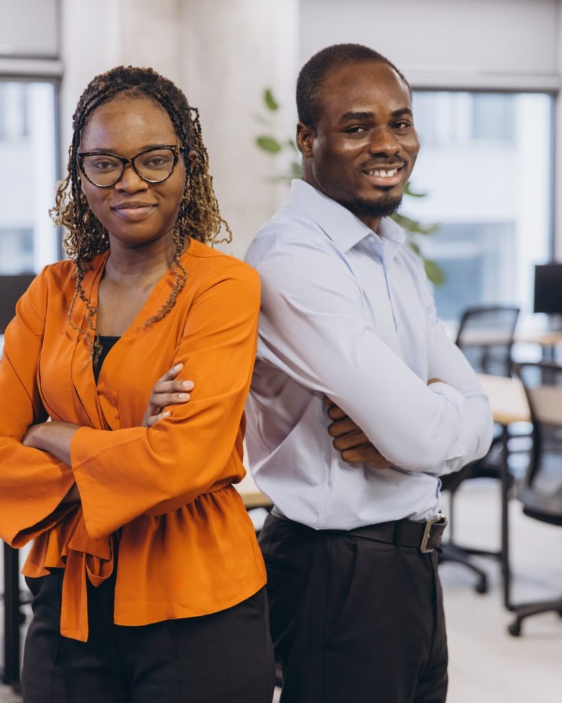 Two african american business professionals standing back to back in a modern office, showcasing teamwork and diversity in a collaborative work environment