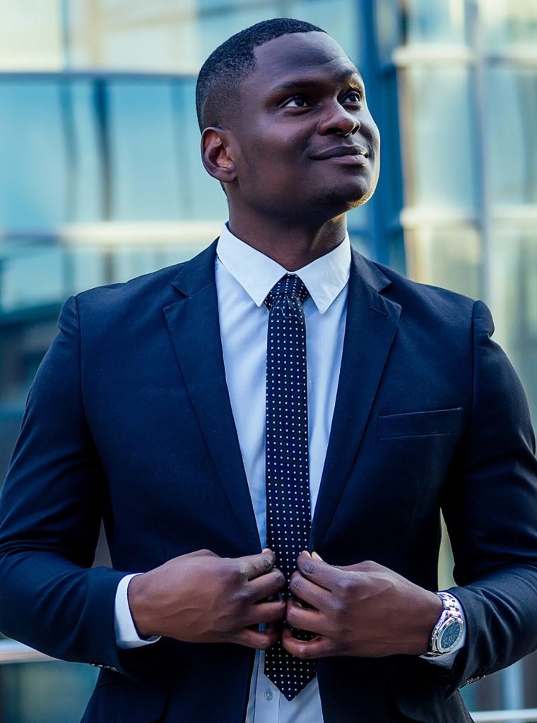 portrait of beautiful and stylish African American man in a fashionable black jacket and a white shirt with a collar with a elegant tie posing background of Manhattan glass offices cityscape